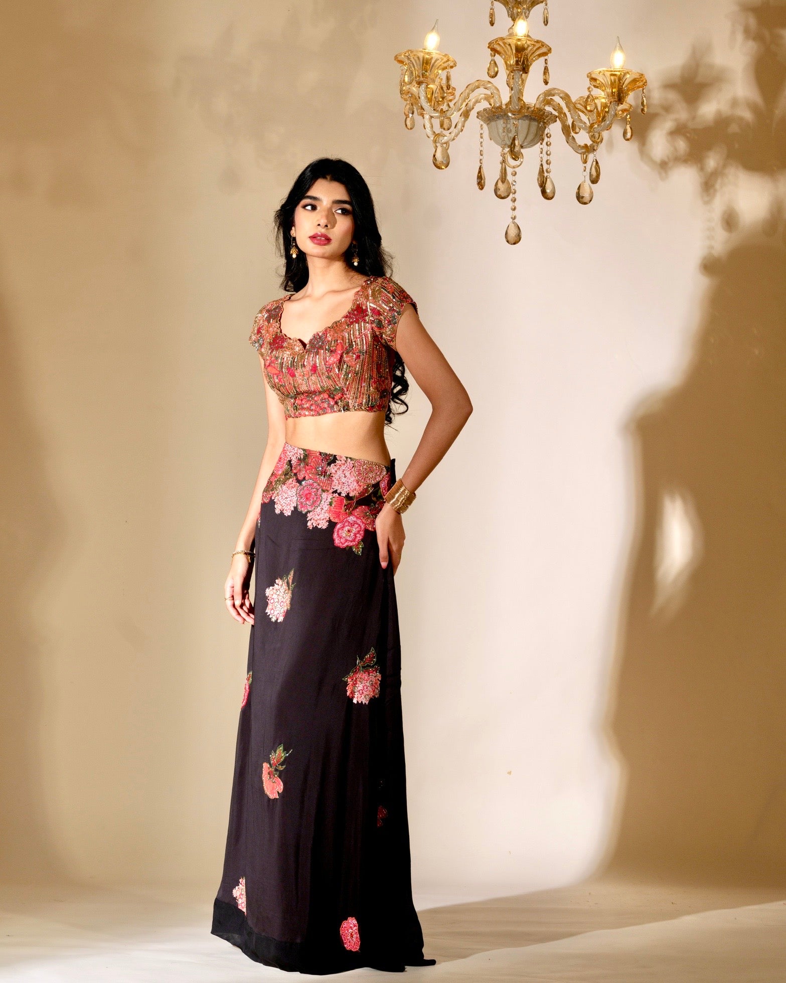 Woman wearing a floral top and black skirt with pink flowers against a beige wall.