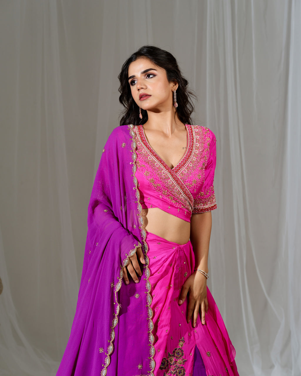Woman wearing a vibrant pink saree with intricate designs against a plain background