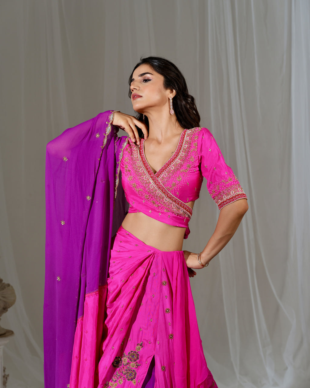 Woman wearing a pink saree with a purple blouse against a plain background