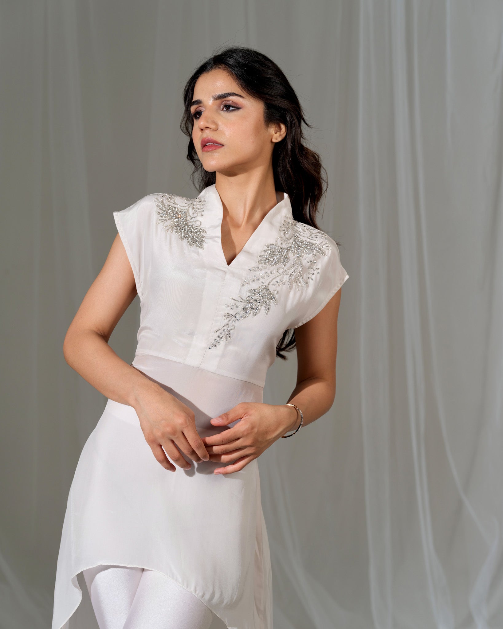 Woman wearing a white dress with intricate detailing on a plain background