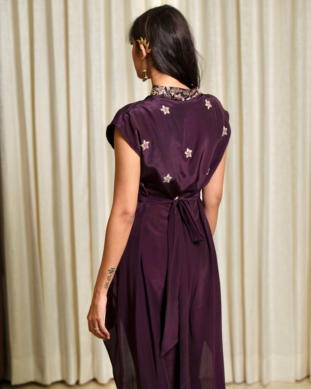 Woman wearing a purple dress with star patterns in front of beige curtains