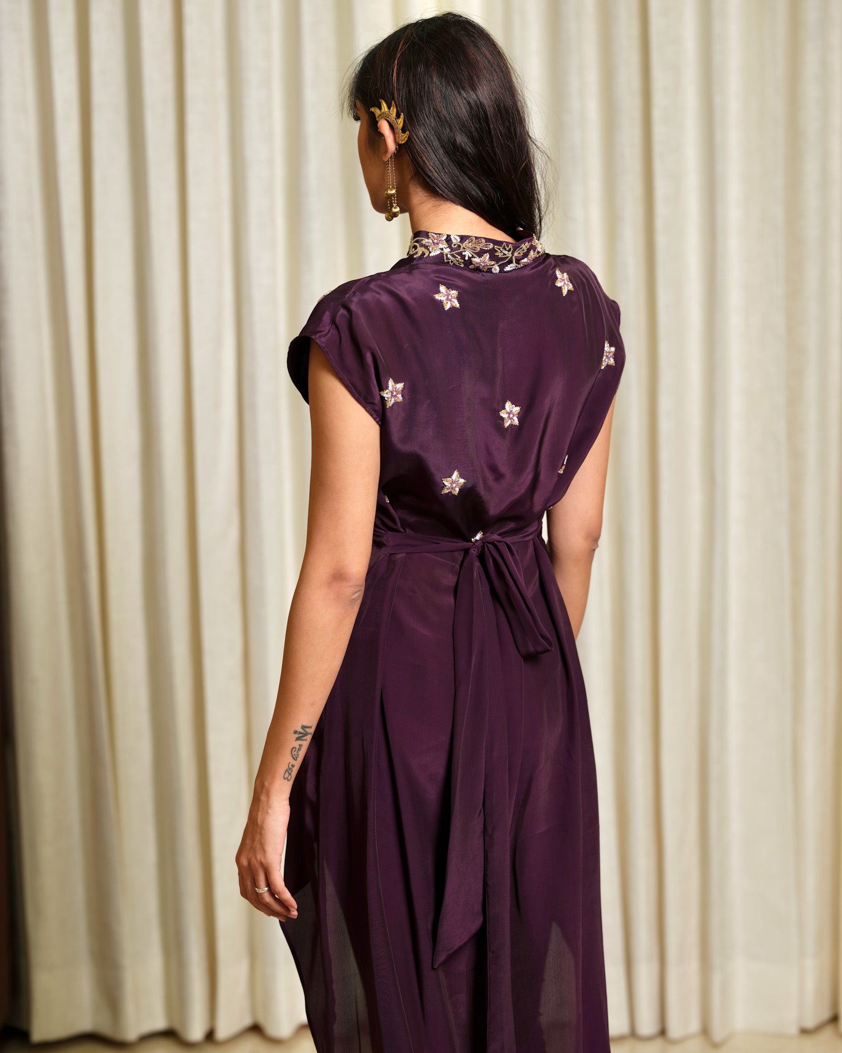 Woman wearing a purple dress with star patterns in front of beige curtains