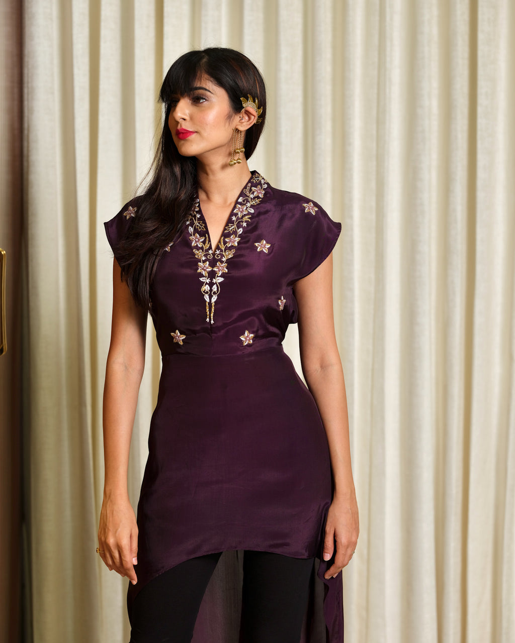Woman wearing a purple embroidered dress against a beige curtain background