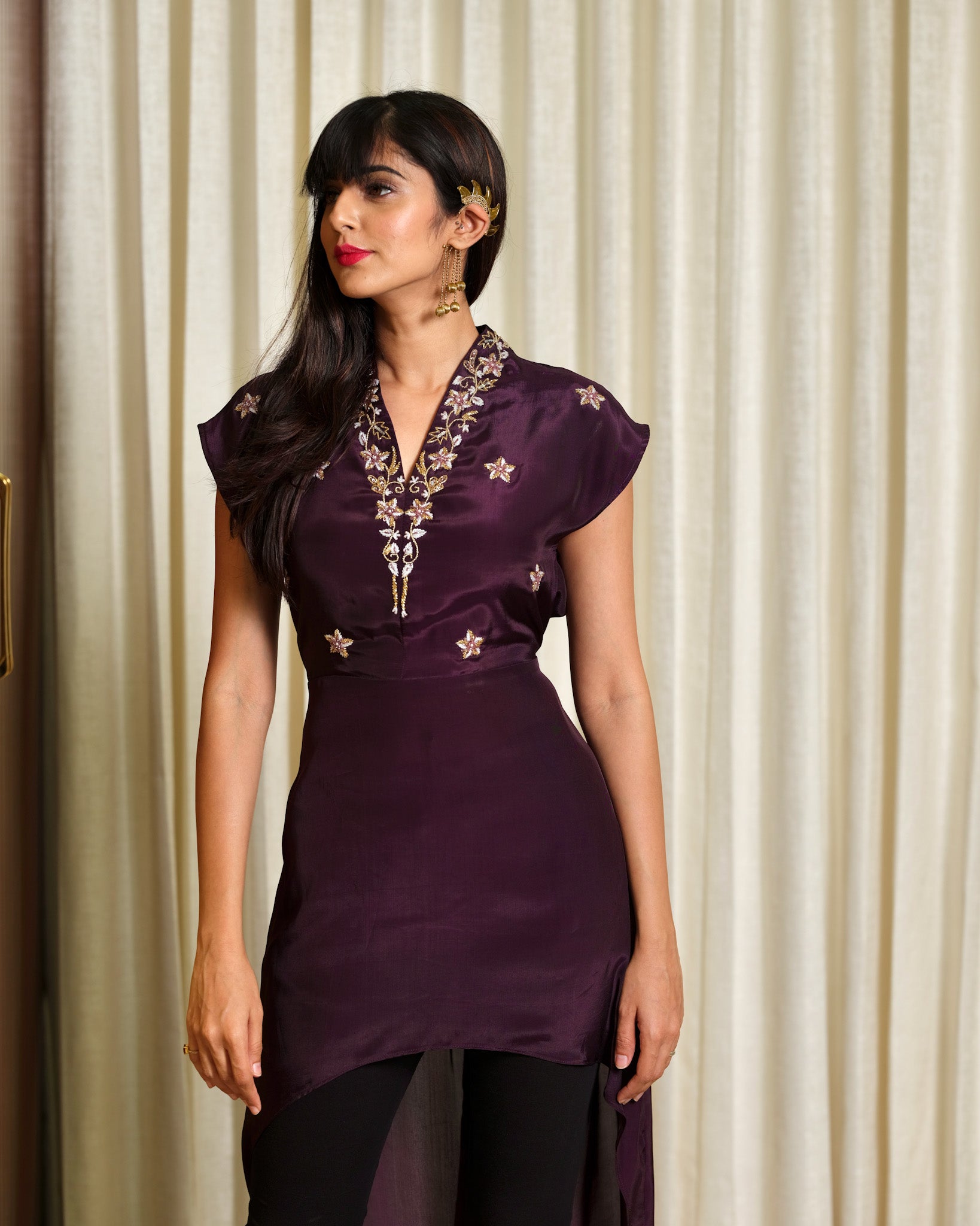 Woman wearing a purple embroidered dress against a beige curtain background