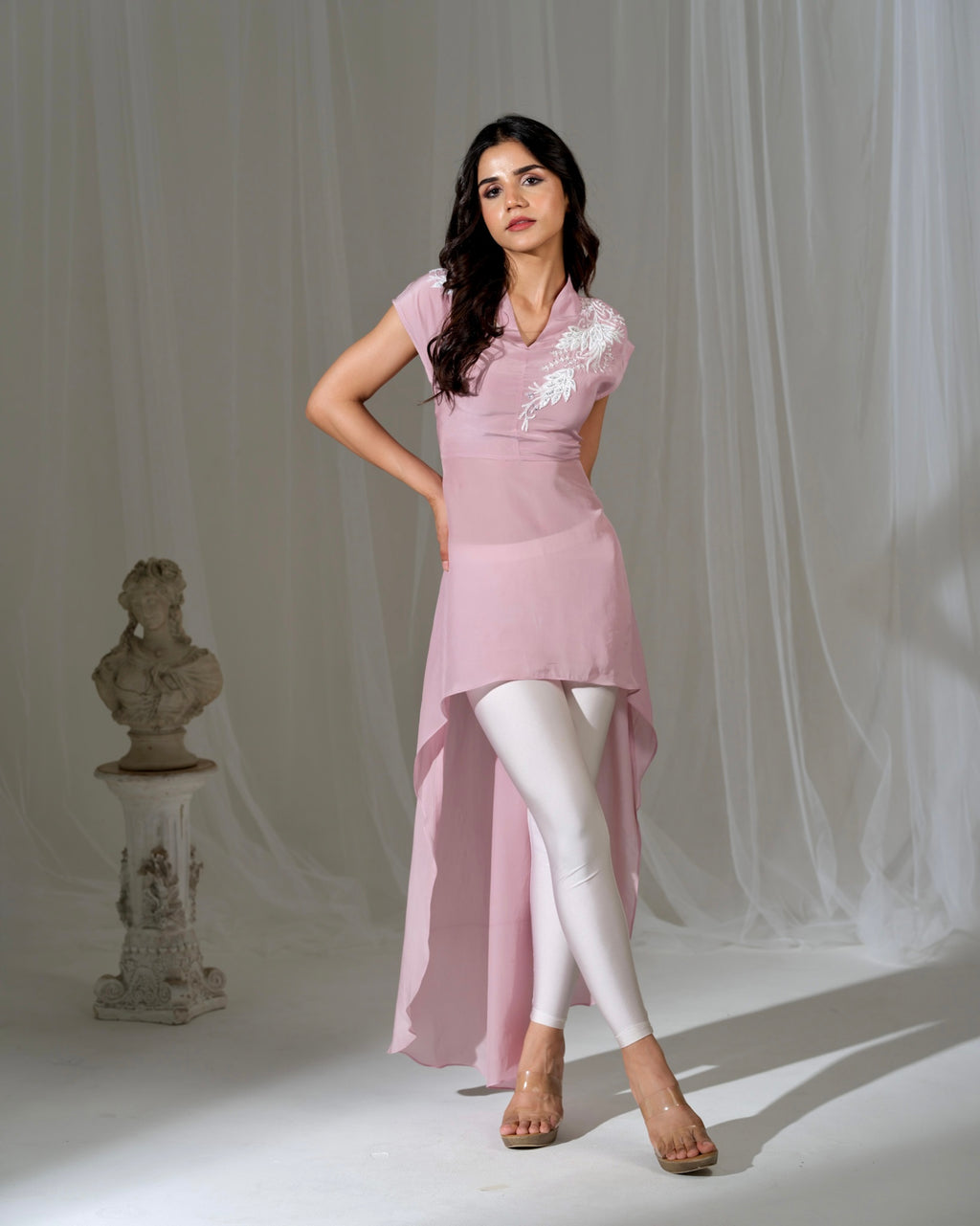 Woman wearing a pink dress with white lace details against a plain background