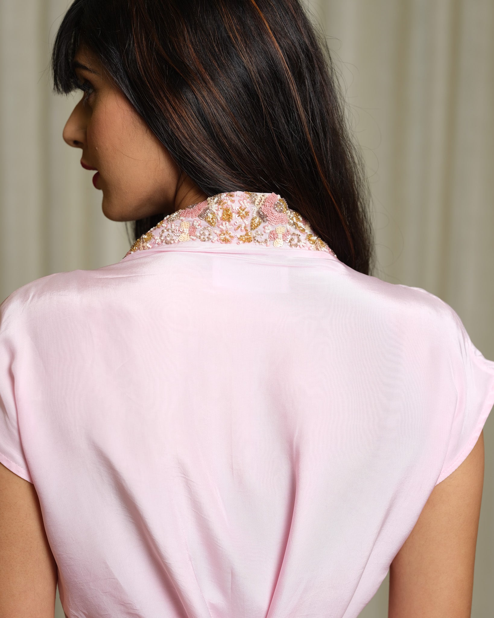 Woman wearing a light pink blouse with an embroidered neckline against a neutral background