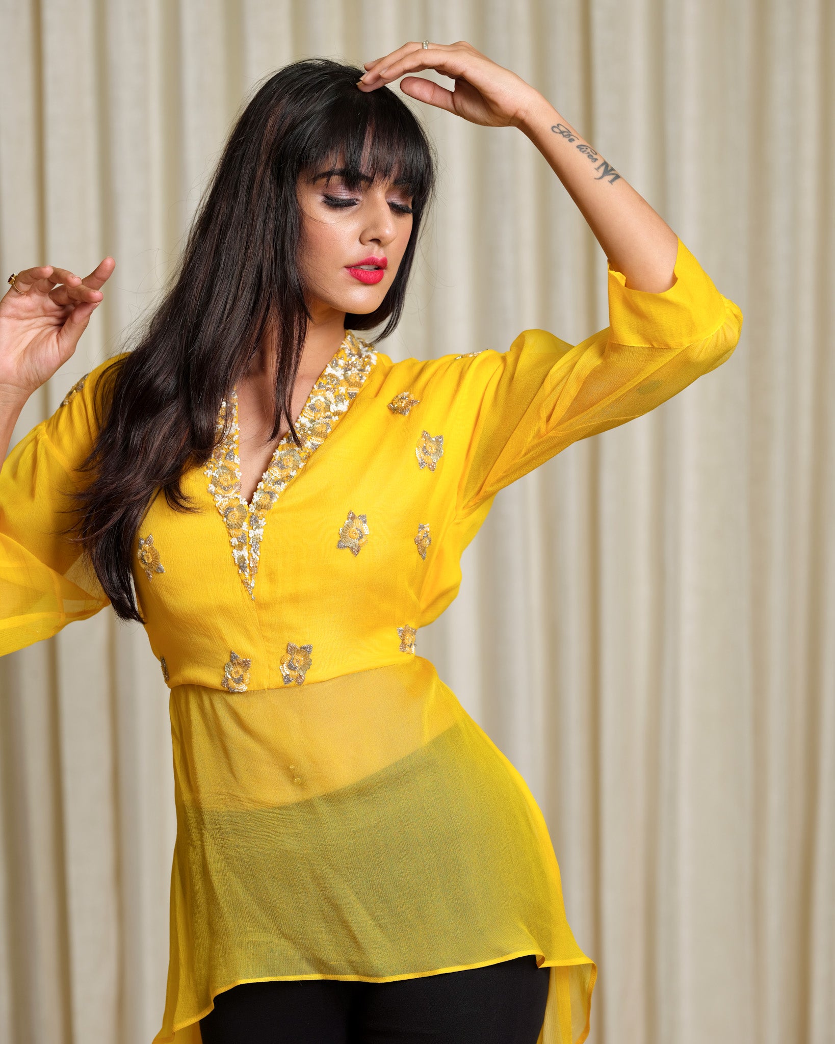 Woman wearing a yellow embroidered top with a plain background