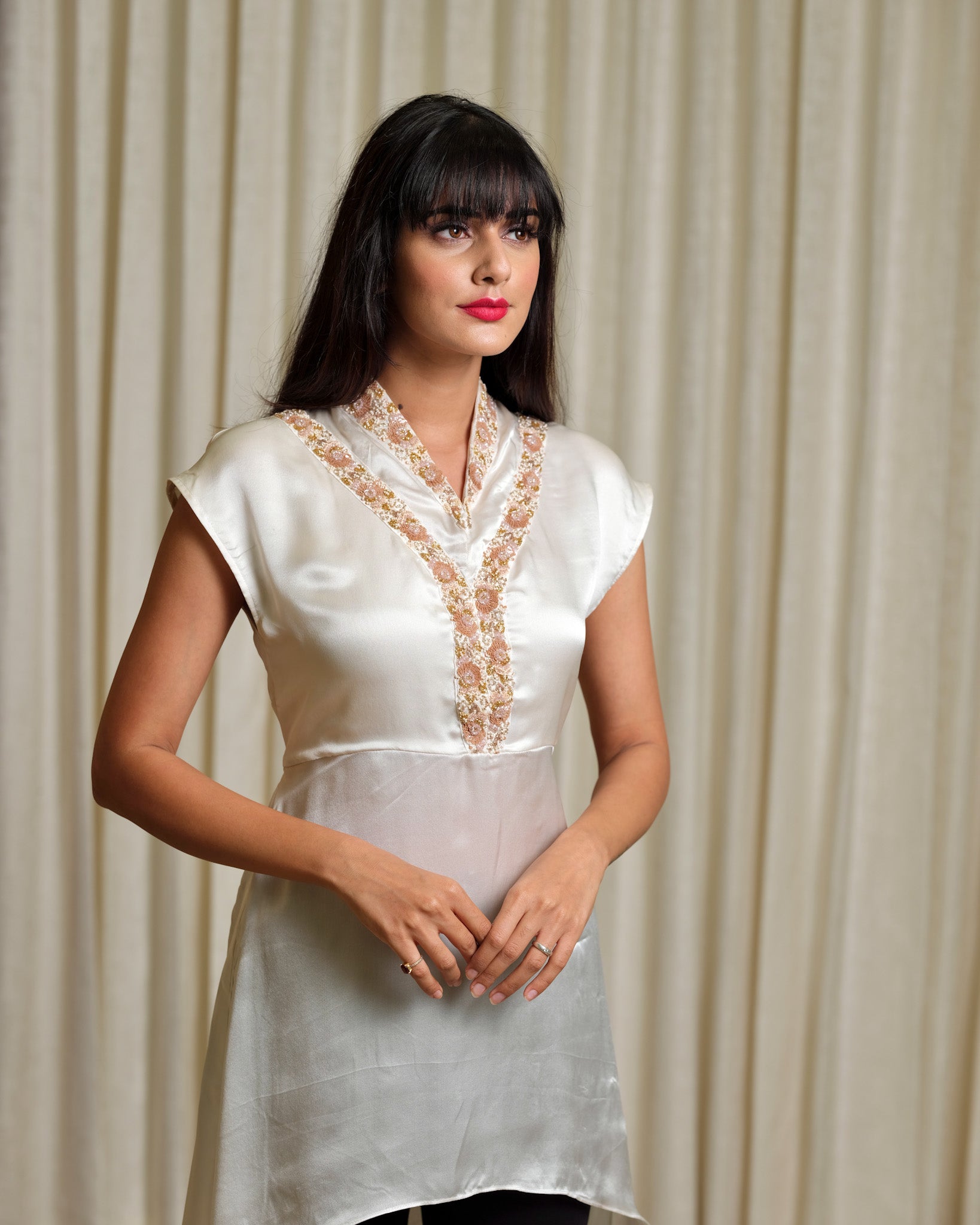 Woman wearing a white embroidered top against a beige curtain background