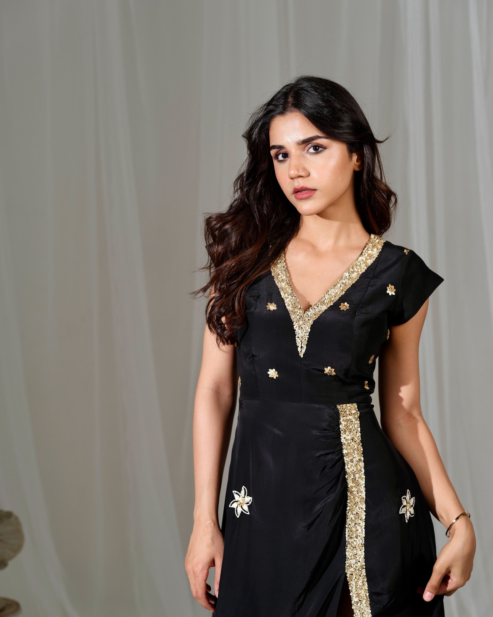 Woman wearing a black dress with gold embroidery against a plain background