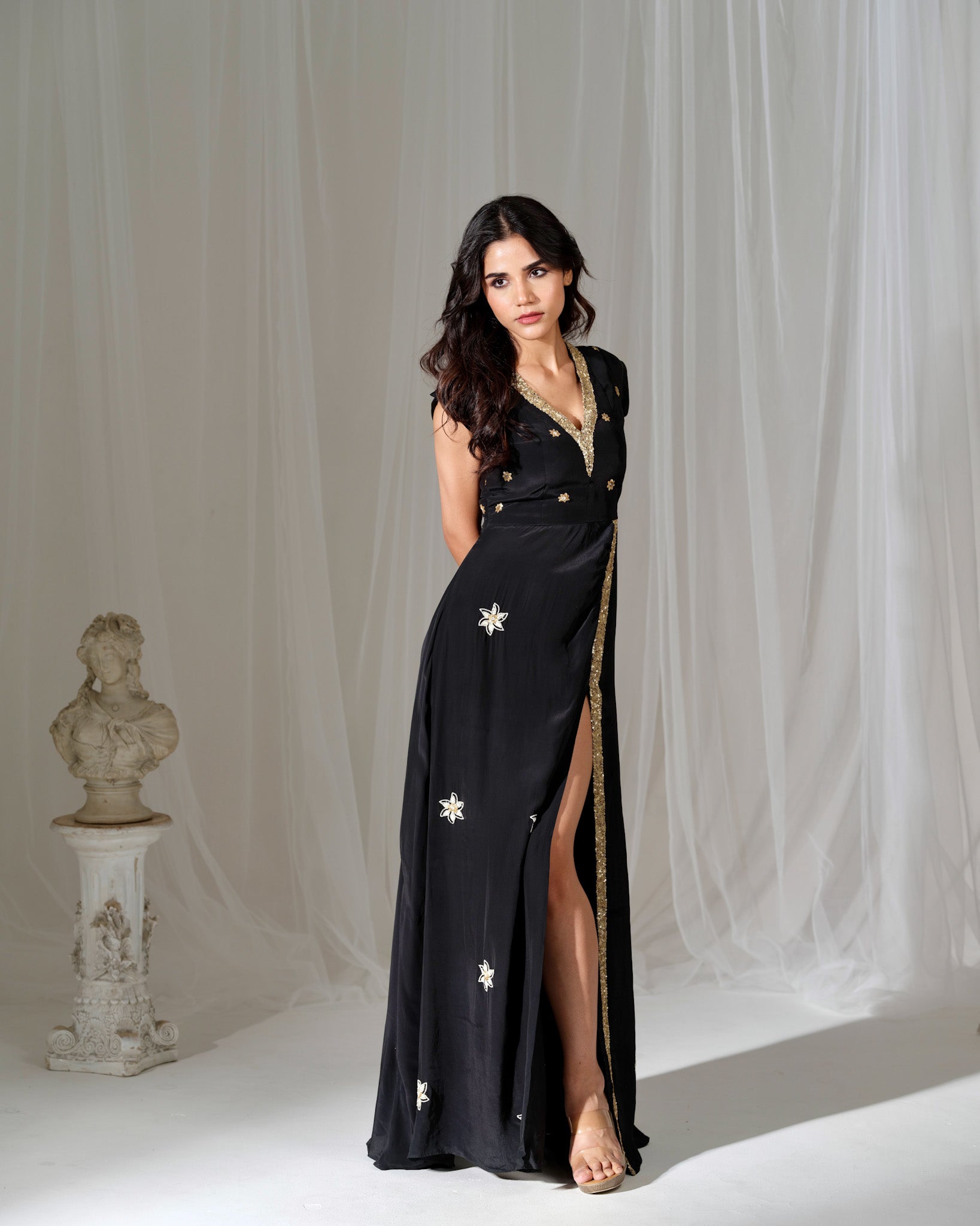 Woman in a black evening gown with star designs standing against a white curtain.
