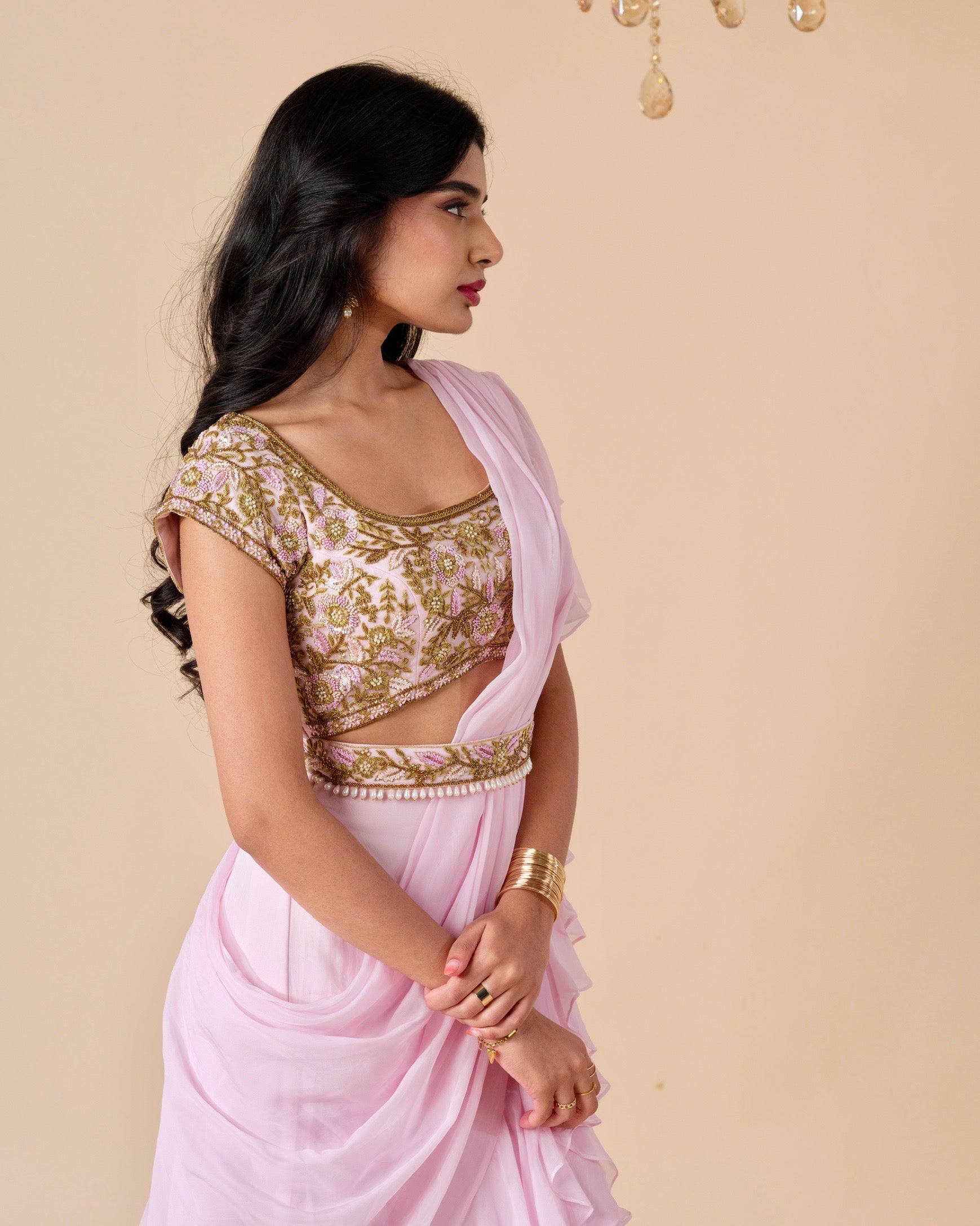 Woman wearing a pink saree with gold blouse against a beige background