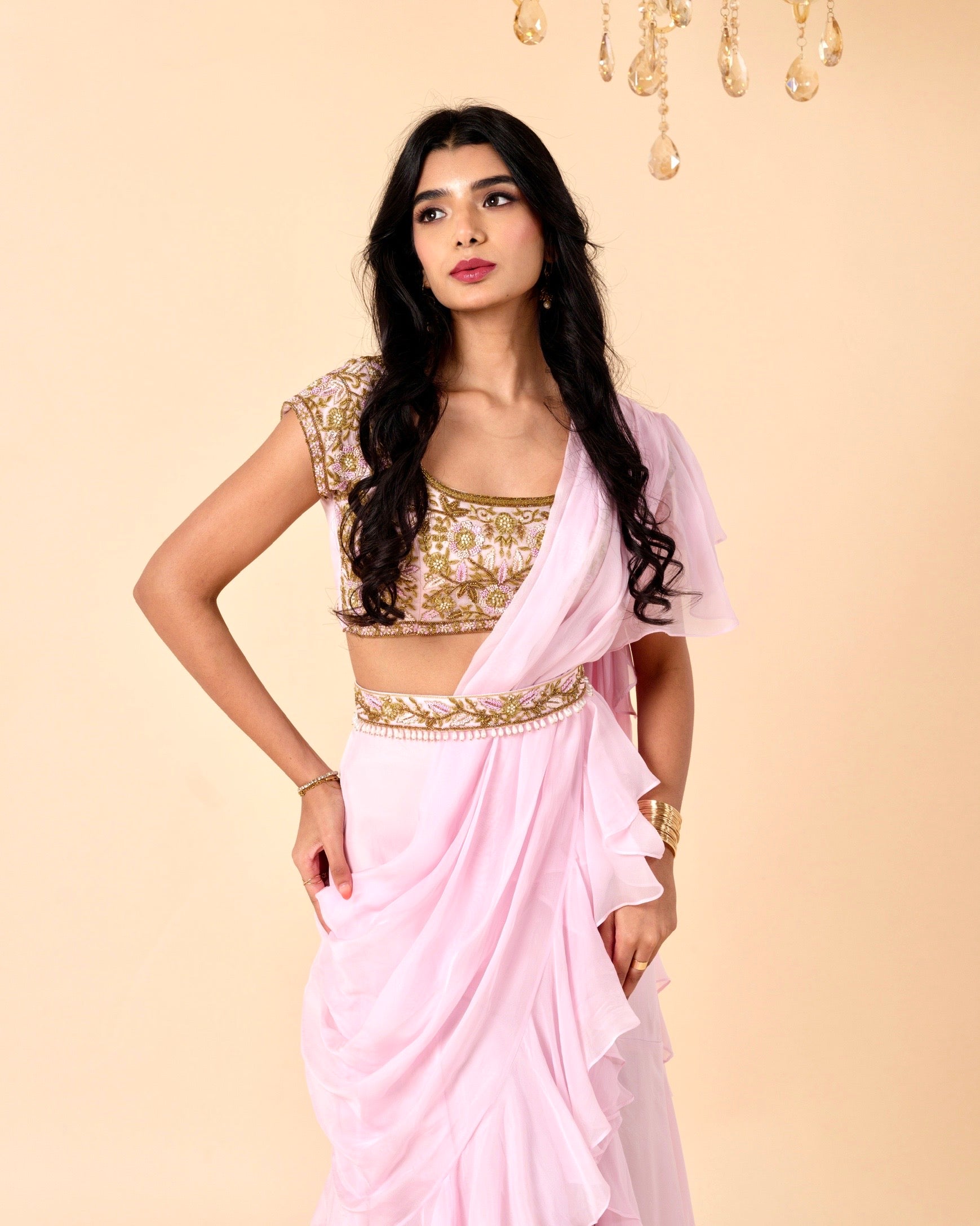Woman wearing a pink saree with gold blouse against a beige background