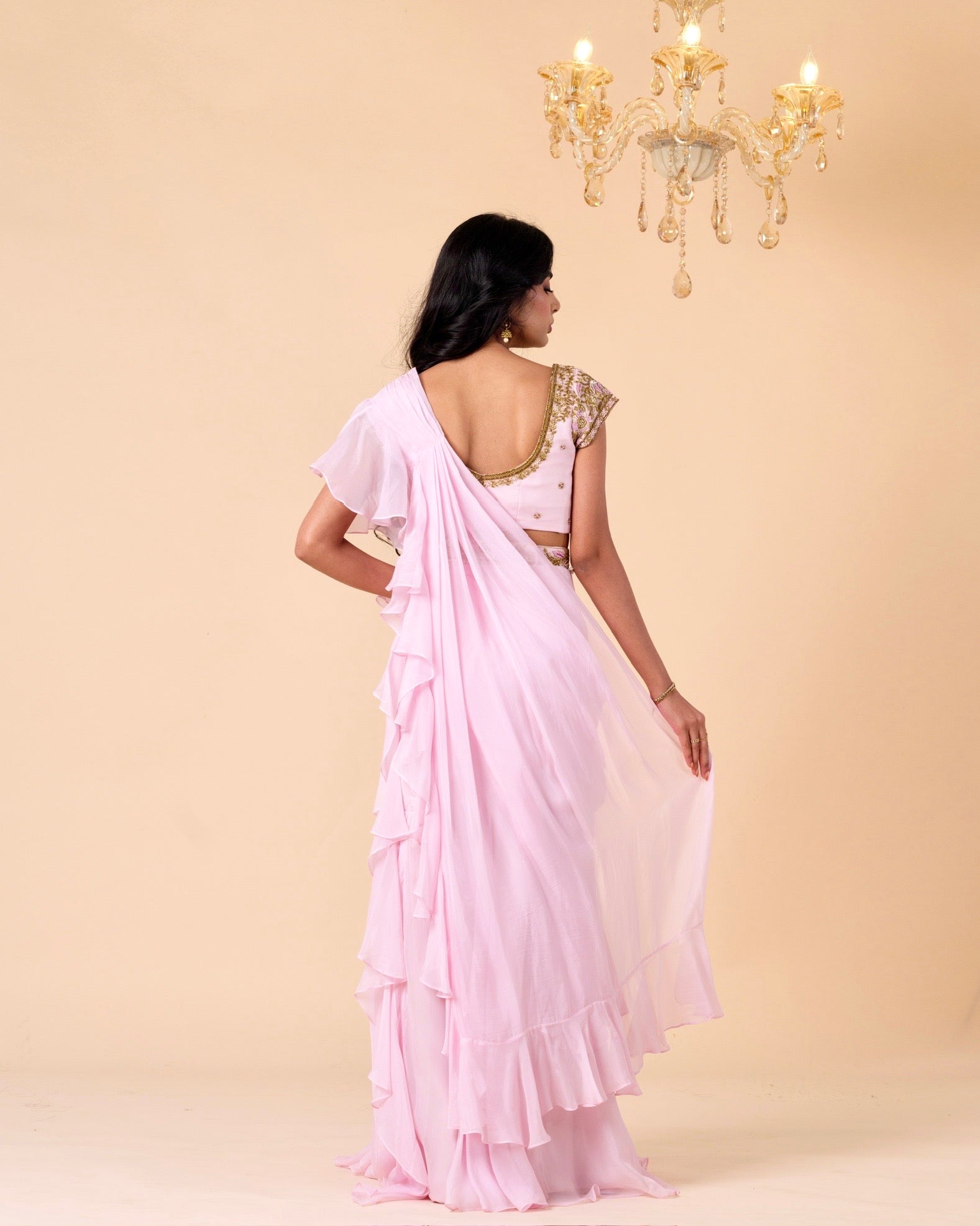 Woman wearing a light pink saree with a gold blouse against a beige background