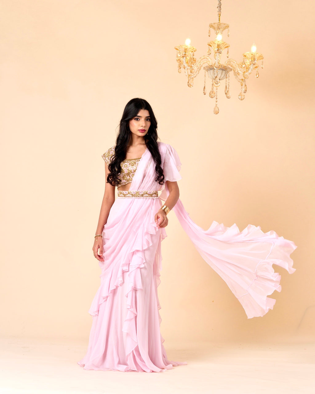 Woman wearing a pink saree with a gold blouse against a beige background