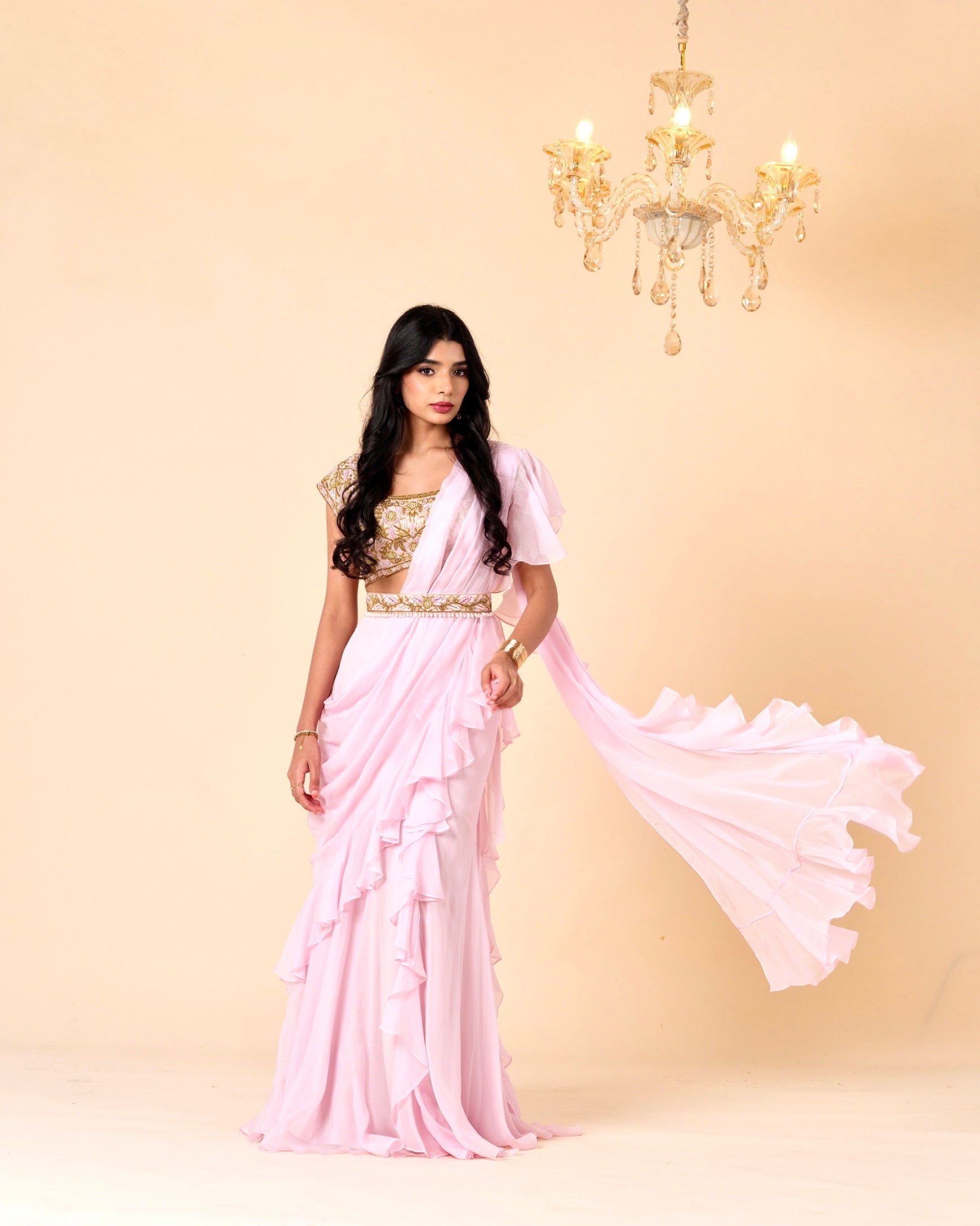 Woman wearing a pink saree with a gold blouse against a beige background