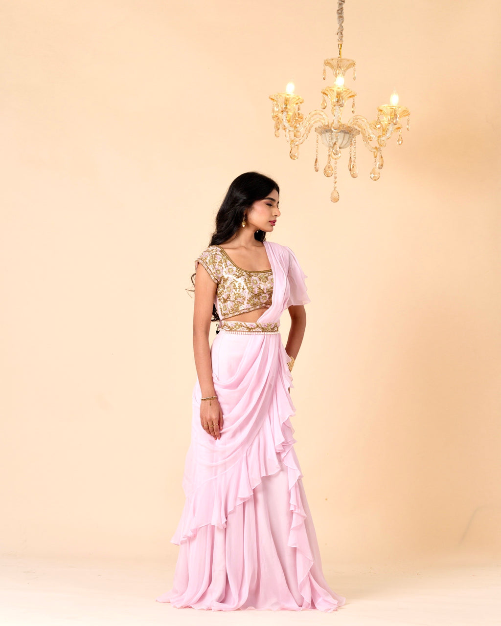 Woman wearing a pink saree with a gold blouse against a beige background