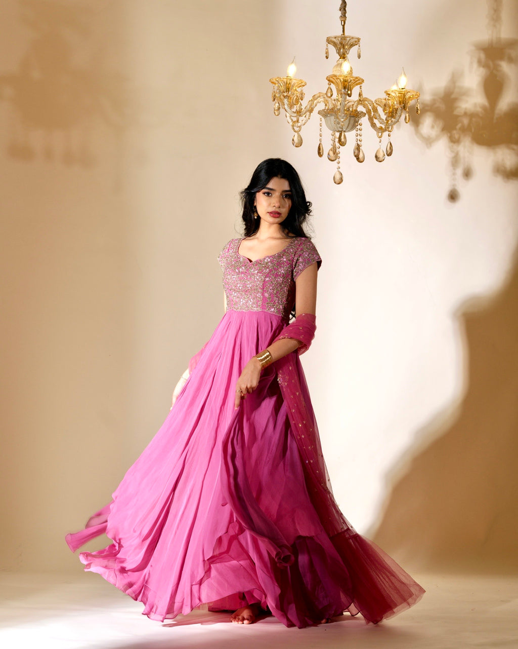 Woman in a pink evening gown standing under a chandelier