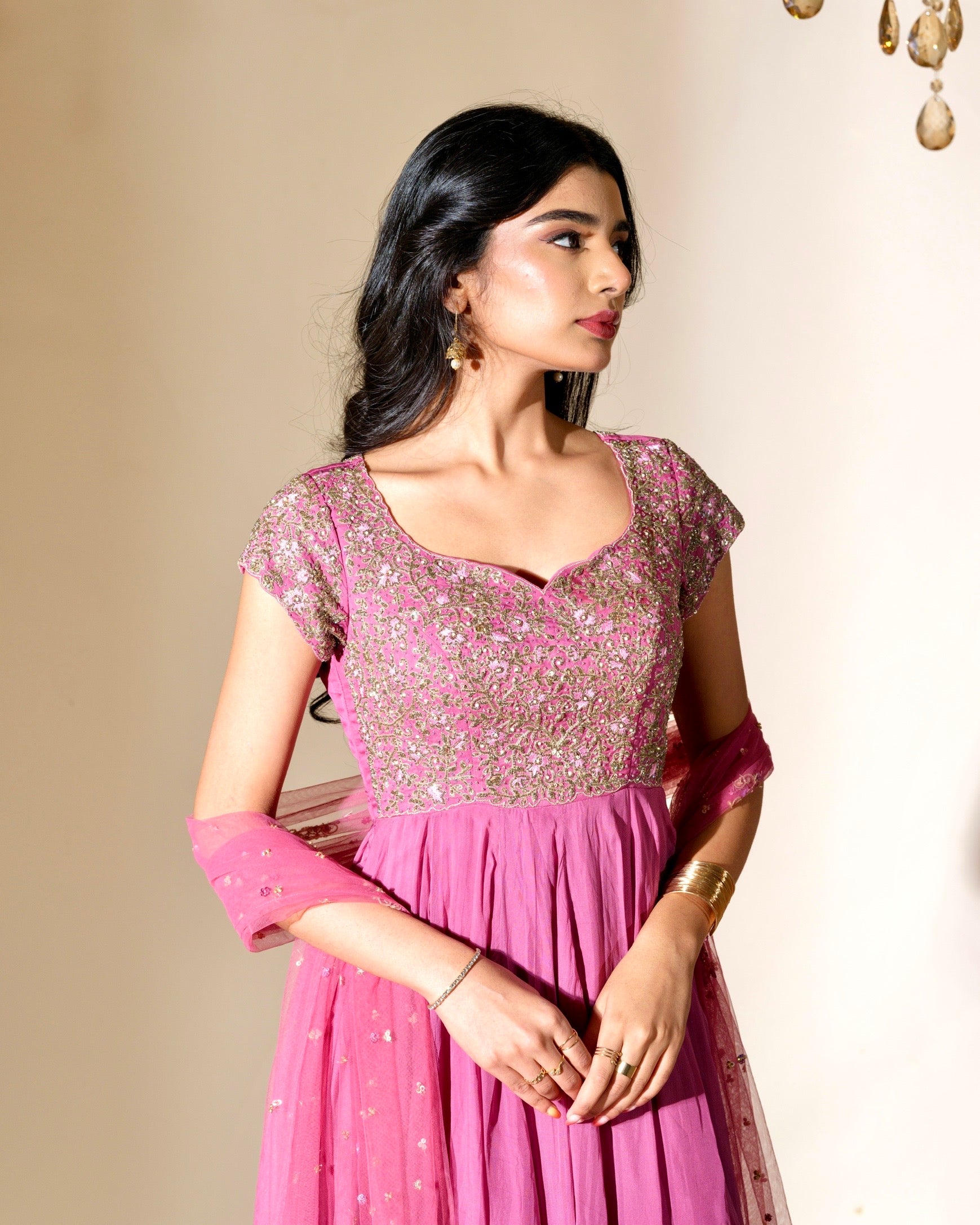 Woman wearing a pink traditional outfit with intricate designs on a beige background
