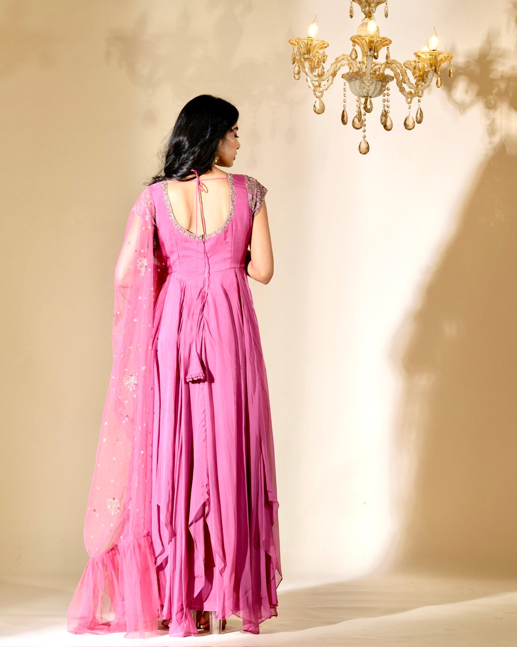 Woman in a pink dress standing in a softly lit room with a chandelier.
