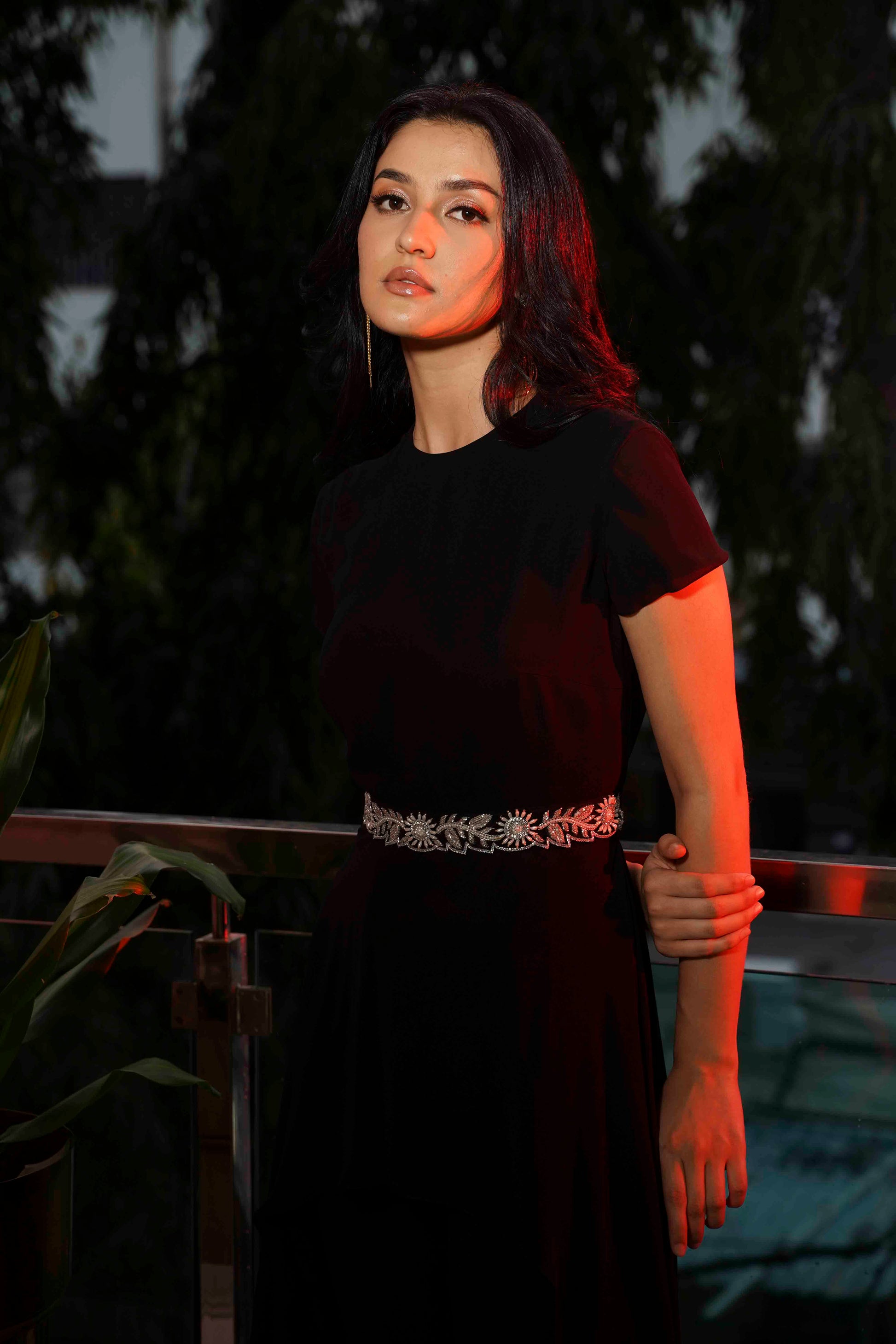 Woman in a black dress with a belt standing outdoors with trees in the background