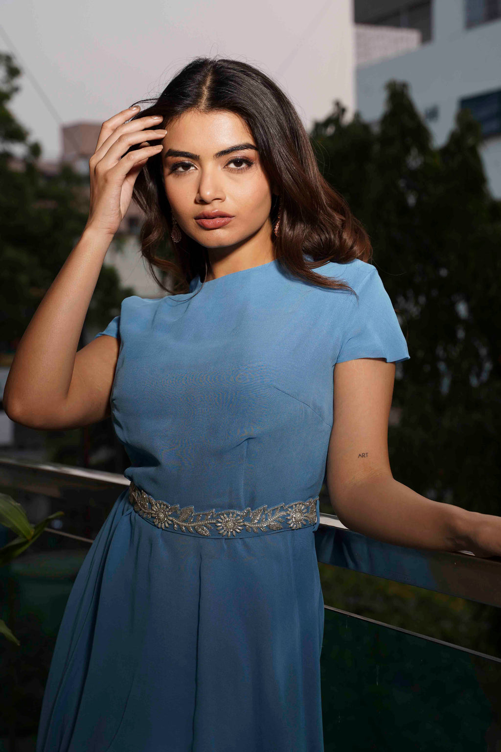 Woman wearing a blue dress with a decorative belt, standing outdoors.