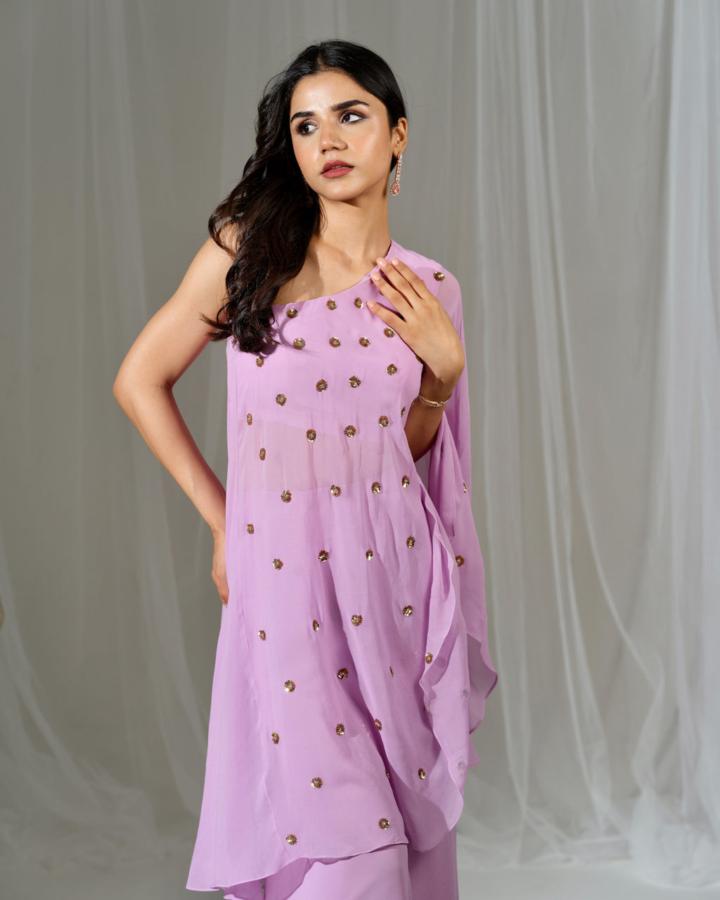 Woman wearing a light purple outfit with gold embellishments against a plain background