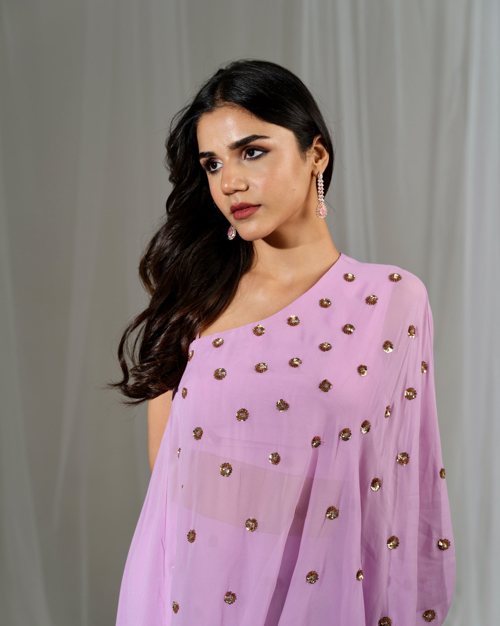 Woman wearing a light purple saree with gold embellishments against a plain background
