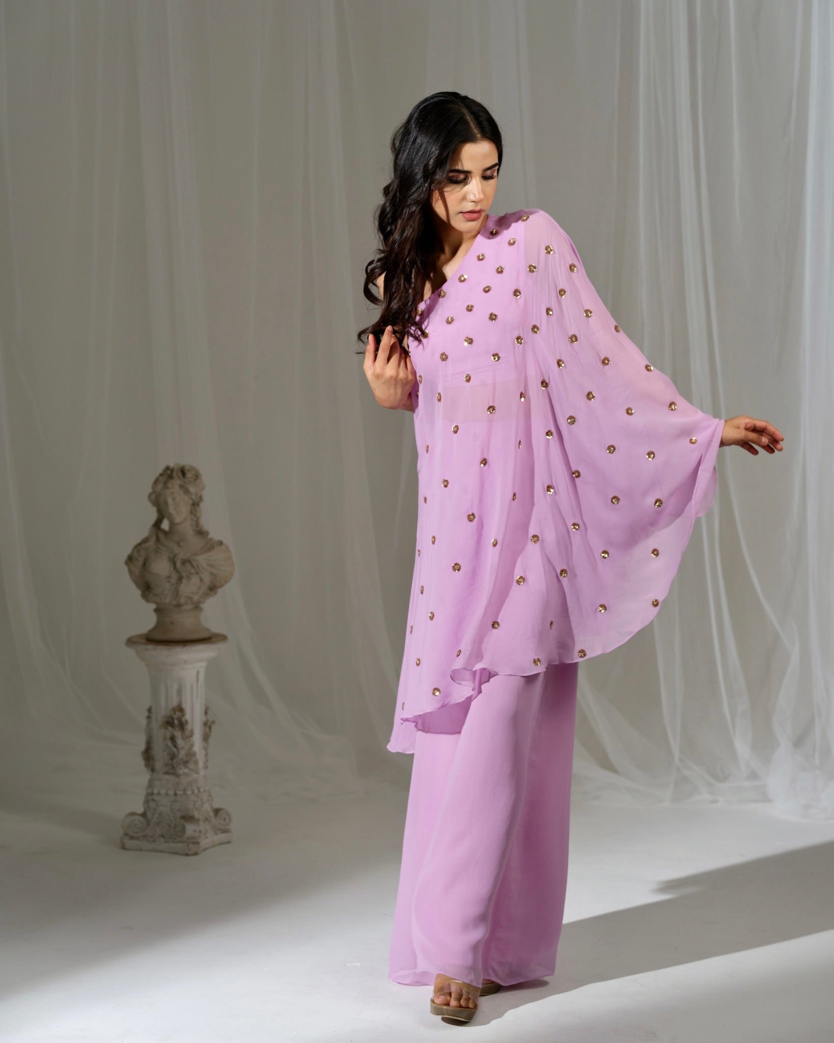Woman in a light purple outfit with a matching dupatta standing against a white curtain.
