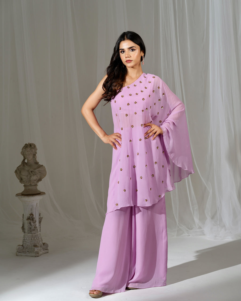 Woman wearing a light pink traditional outfit with a white curtain background