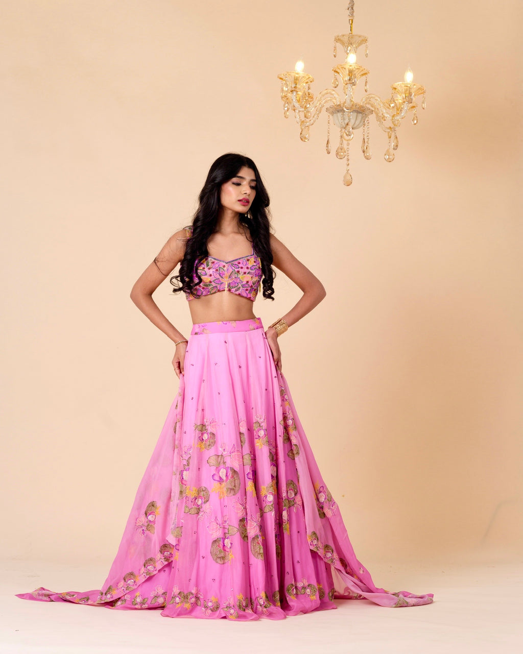 Woman wearing a pink traditional outfit with floral patterns in a well-lit room.