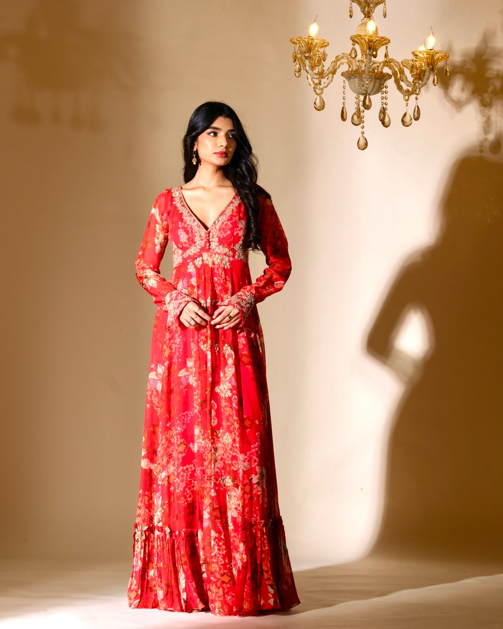 Woman wearing a red floral dress standing in front of a chandelier.