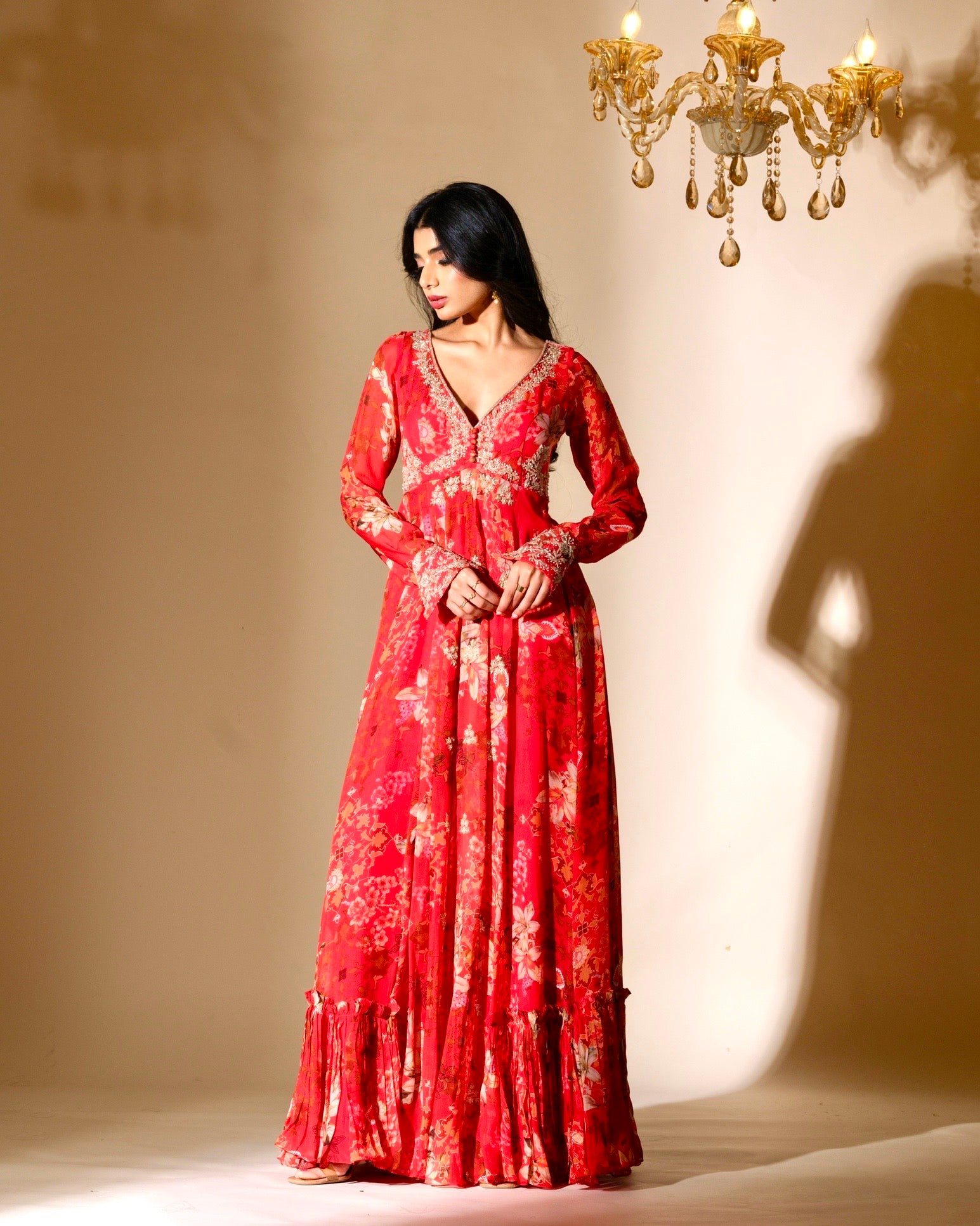 Woman wearing a red floral dress standing in front of a chandelier.