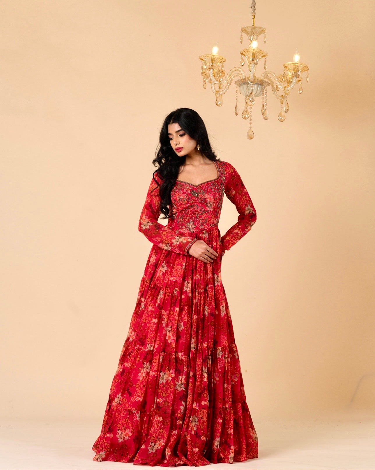Woman wearing a red floral dress against a beige background with a chandelier.