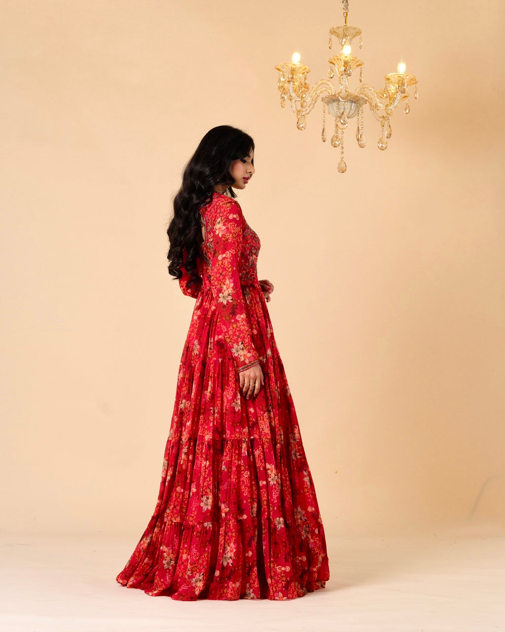Woman in a red floral dress standing in front of a beige wall with a chandelier.