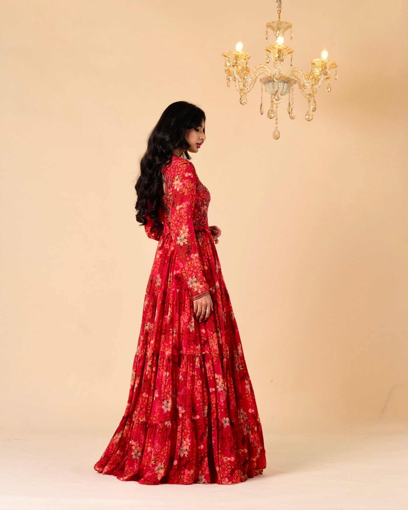Woman in a red floral dress standing in front of a beige wall with a chandelier.