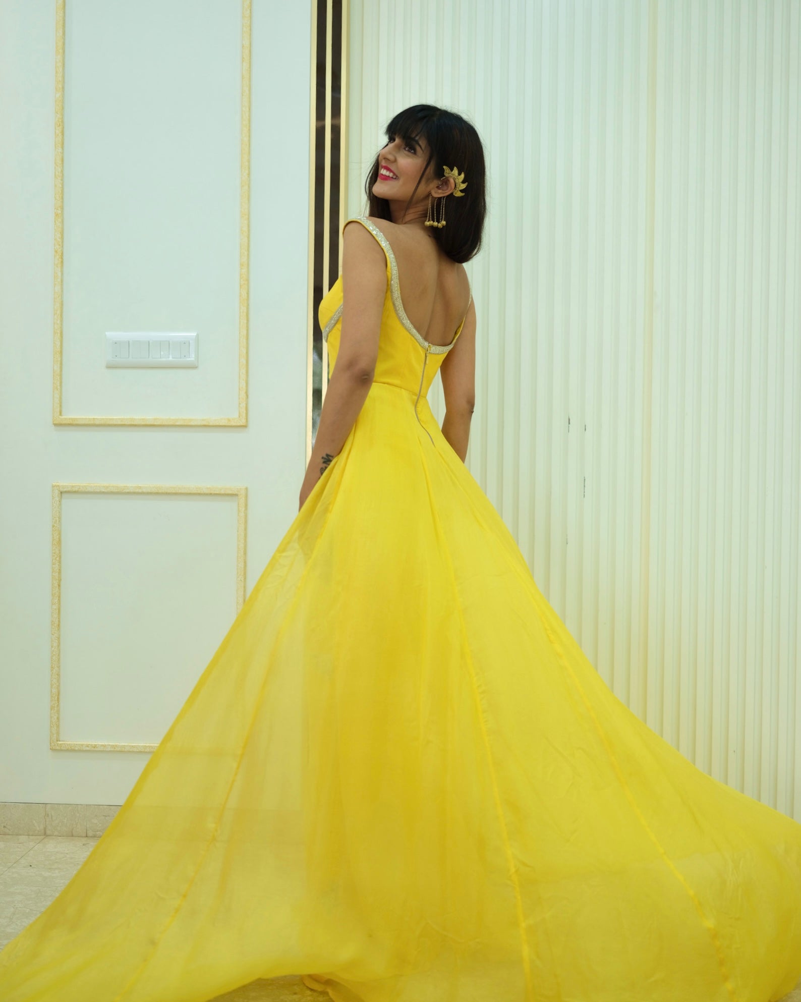 Woman in a yellow dress standing against a white wall.
