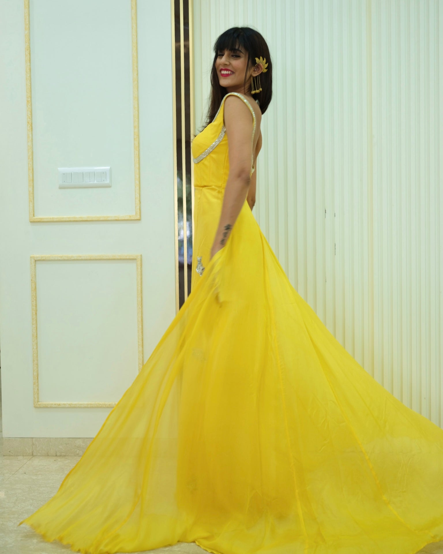 Woman in a yellow dress standing indoors with a neutral background