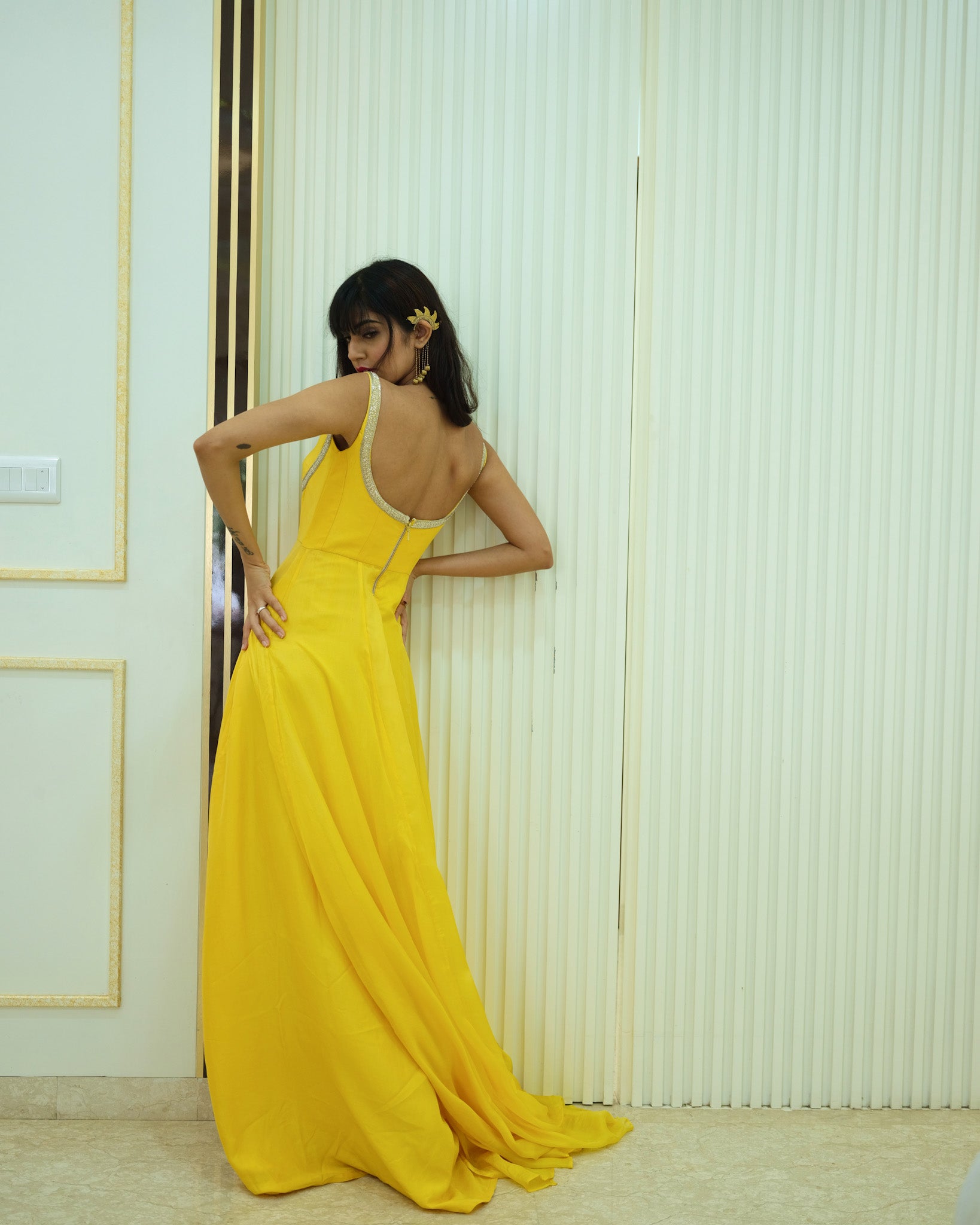 Woman in a yellow evening gown standing against a white wall.