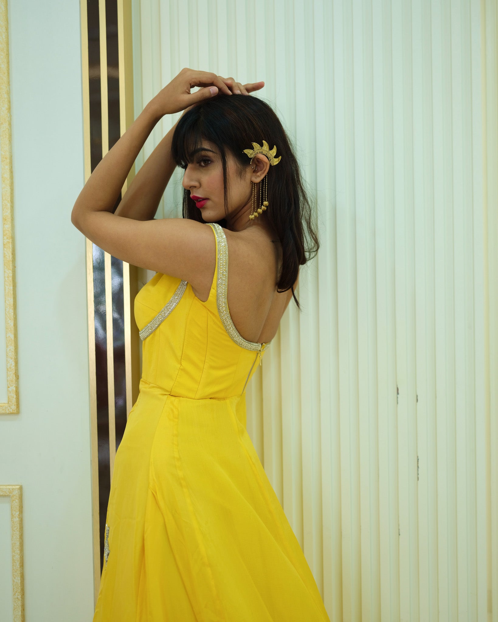 Woman in a yellow dress standing against a light-colored wall.