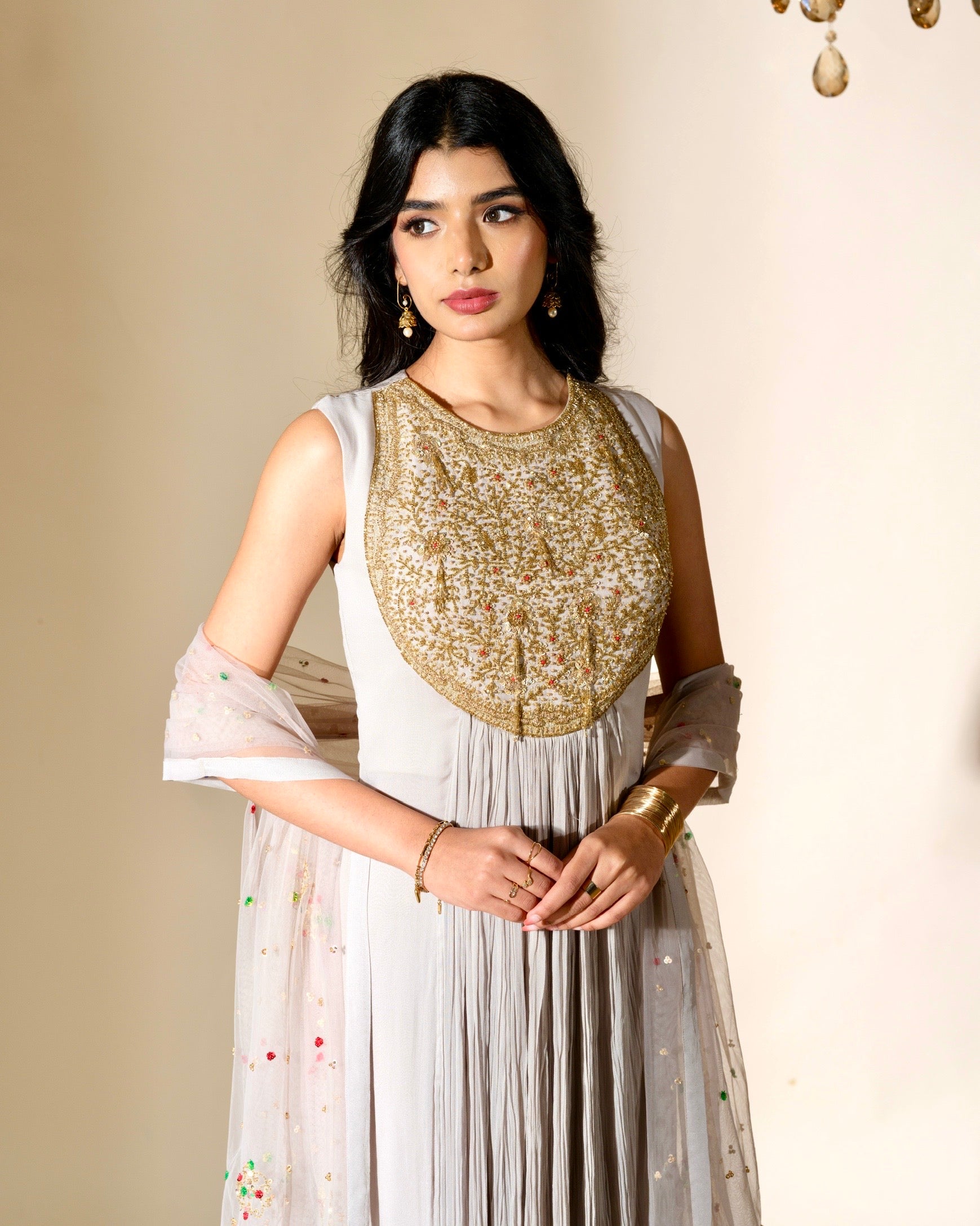 Woman wearing a white dress with a gold embroidered top against a beige background
