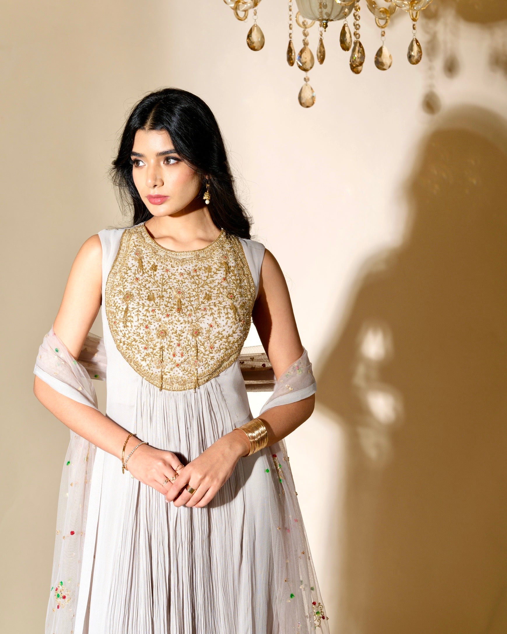 Woman wearing a traditional outfit with a gold embroidered top and white skirt against a neutral background.