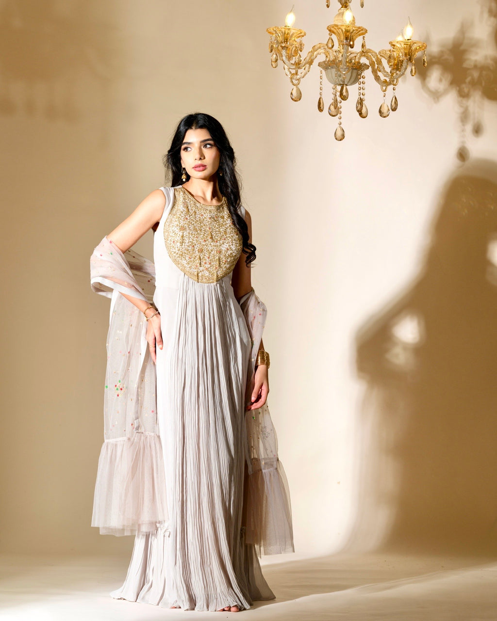 Woman in a white and gold dress standing in front of a chandelier