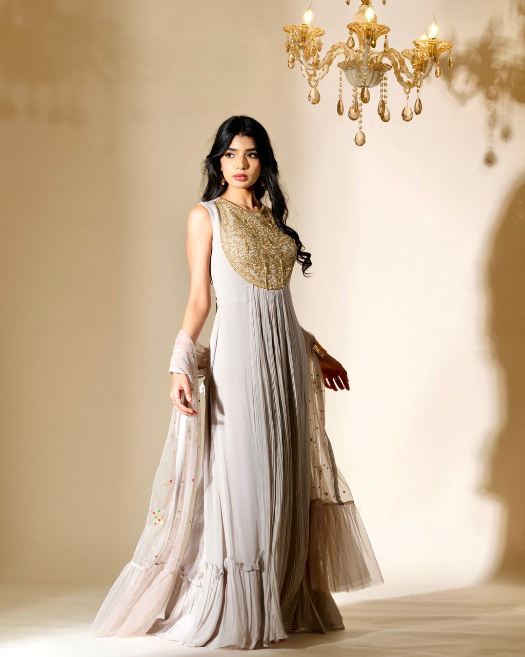 Woman in a white and gold traditional outfit standing in a softly lit room with a chandelier.