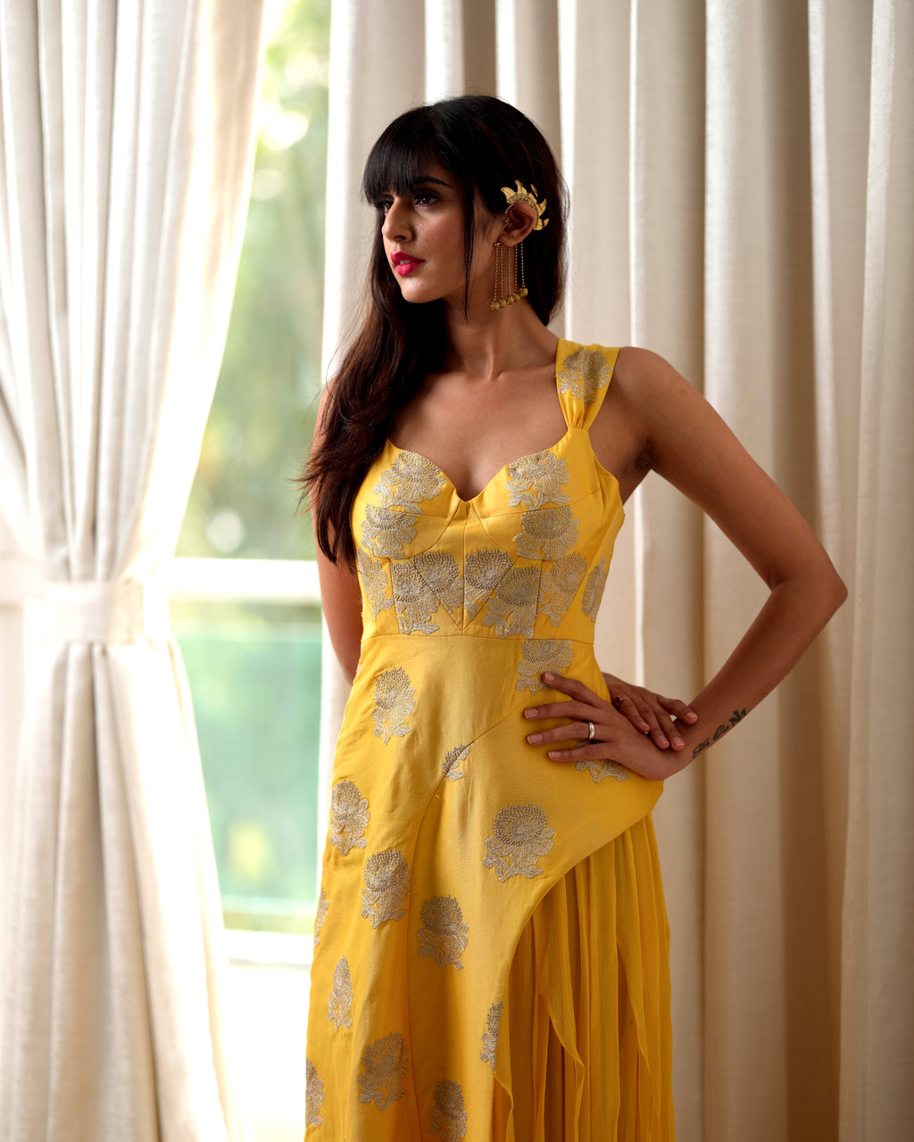 Woman wearing a yellow floral dress standing in front of white curtains.