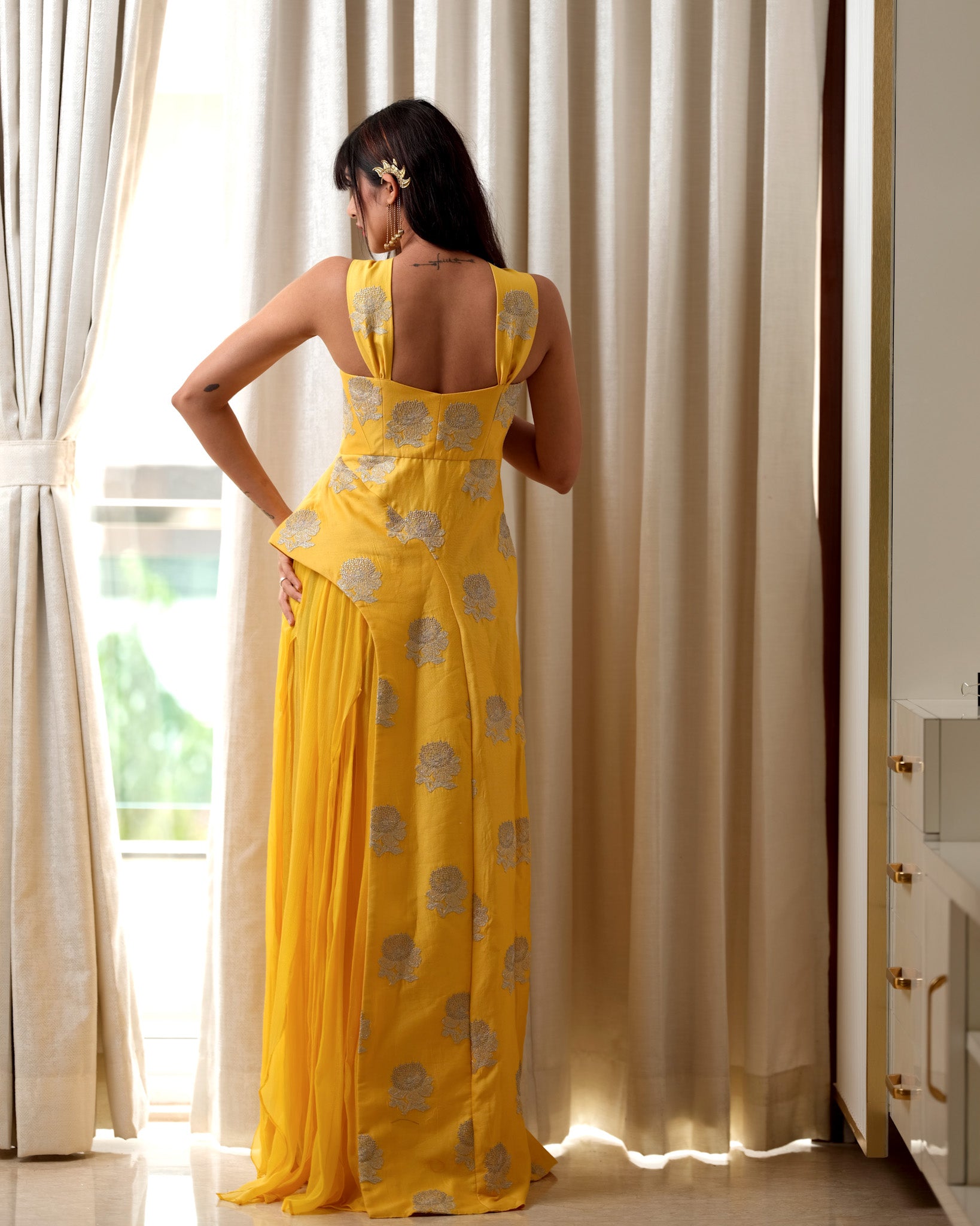 Woman in a yellow dress standing in a room with white curtains.