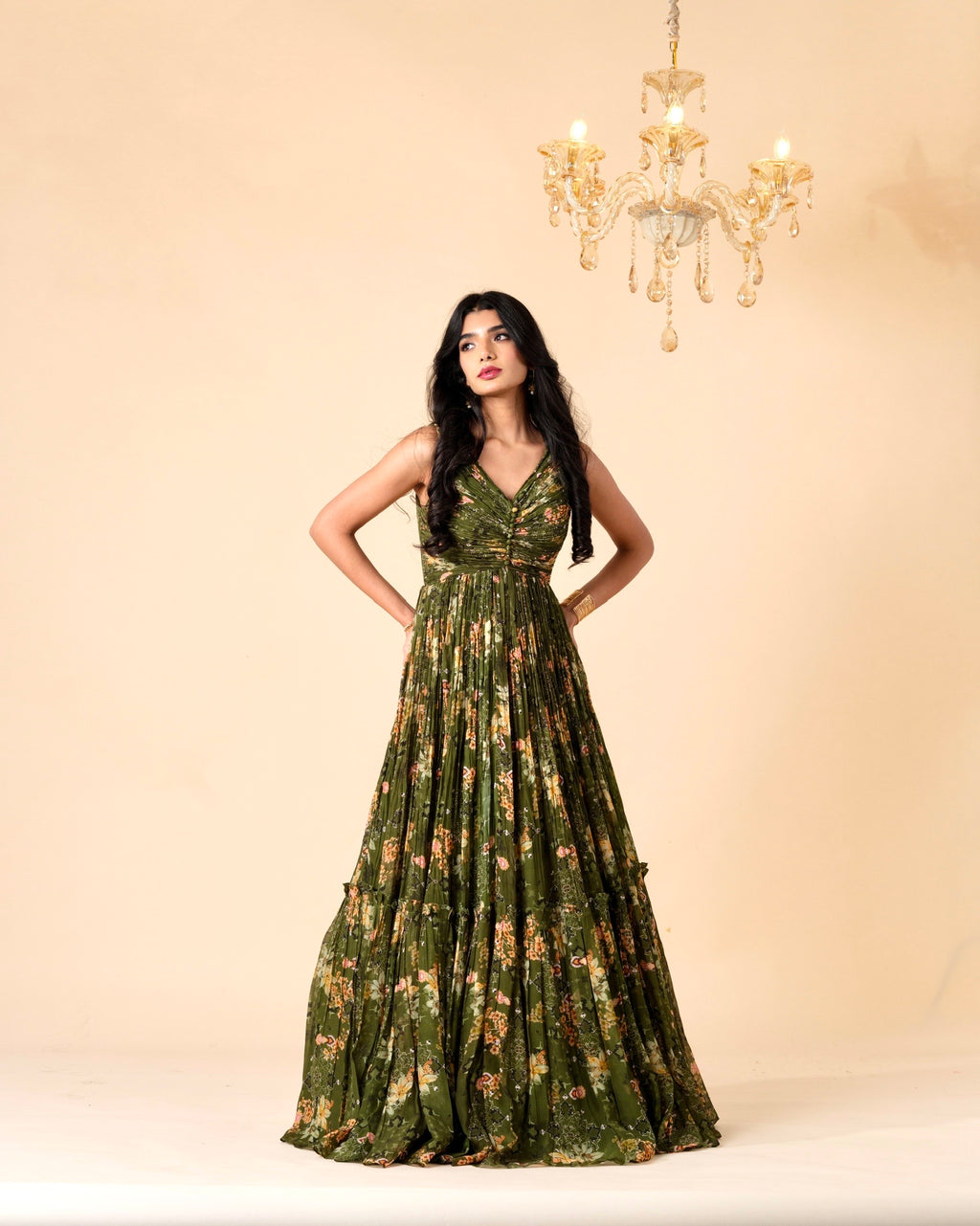 Woman wearing a green floral dress against a beige background with a chandelier.