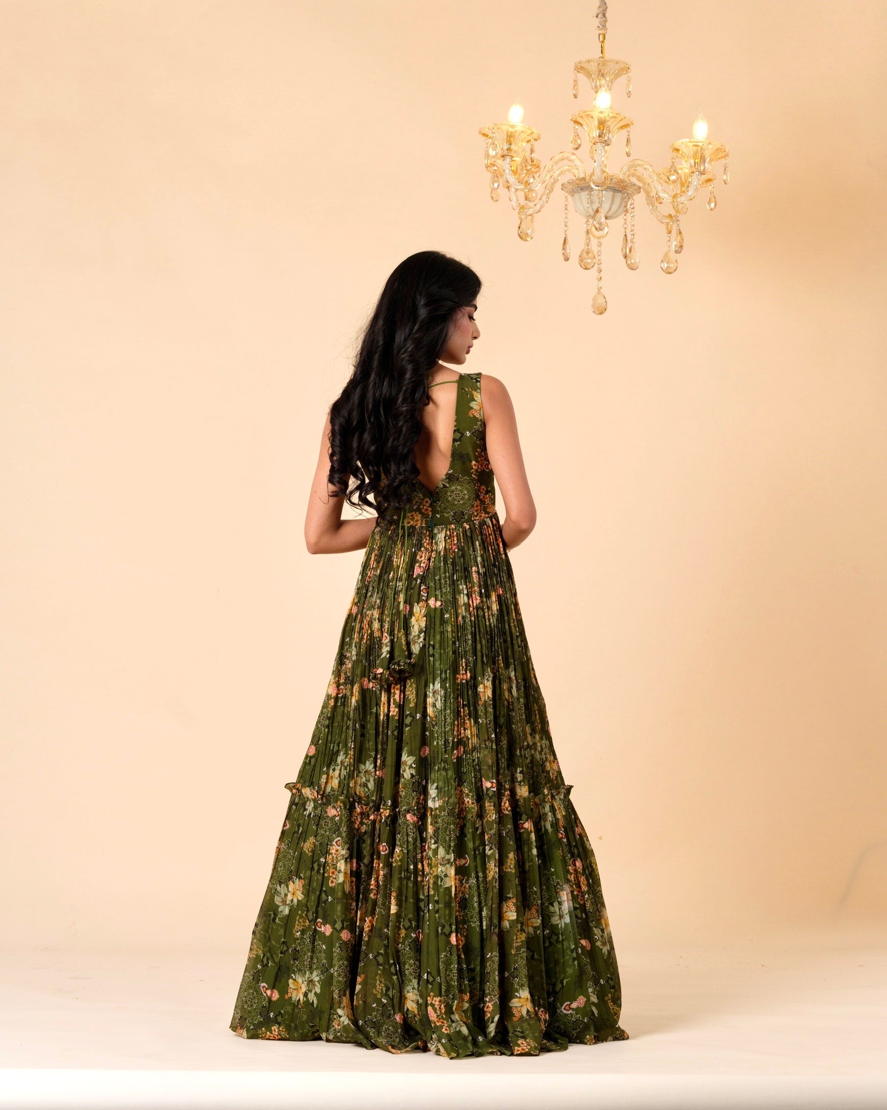 Woman wearing a green floral dress against a beige background with a chandelier.