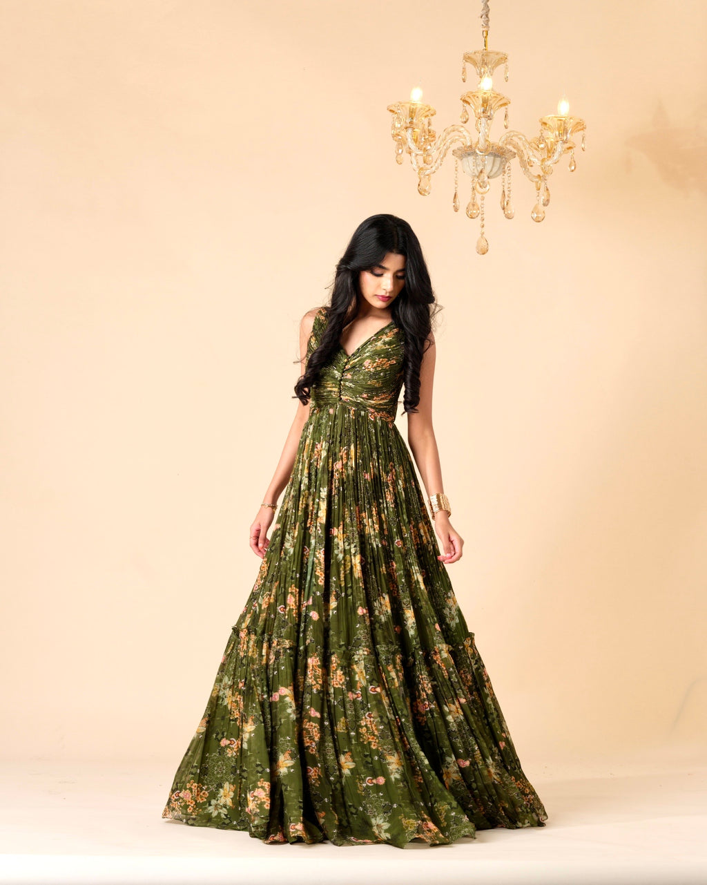 Woman wearing a green floral dress against a beige background with a chandelier.