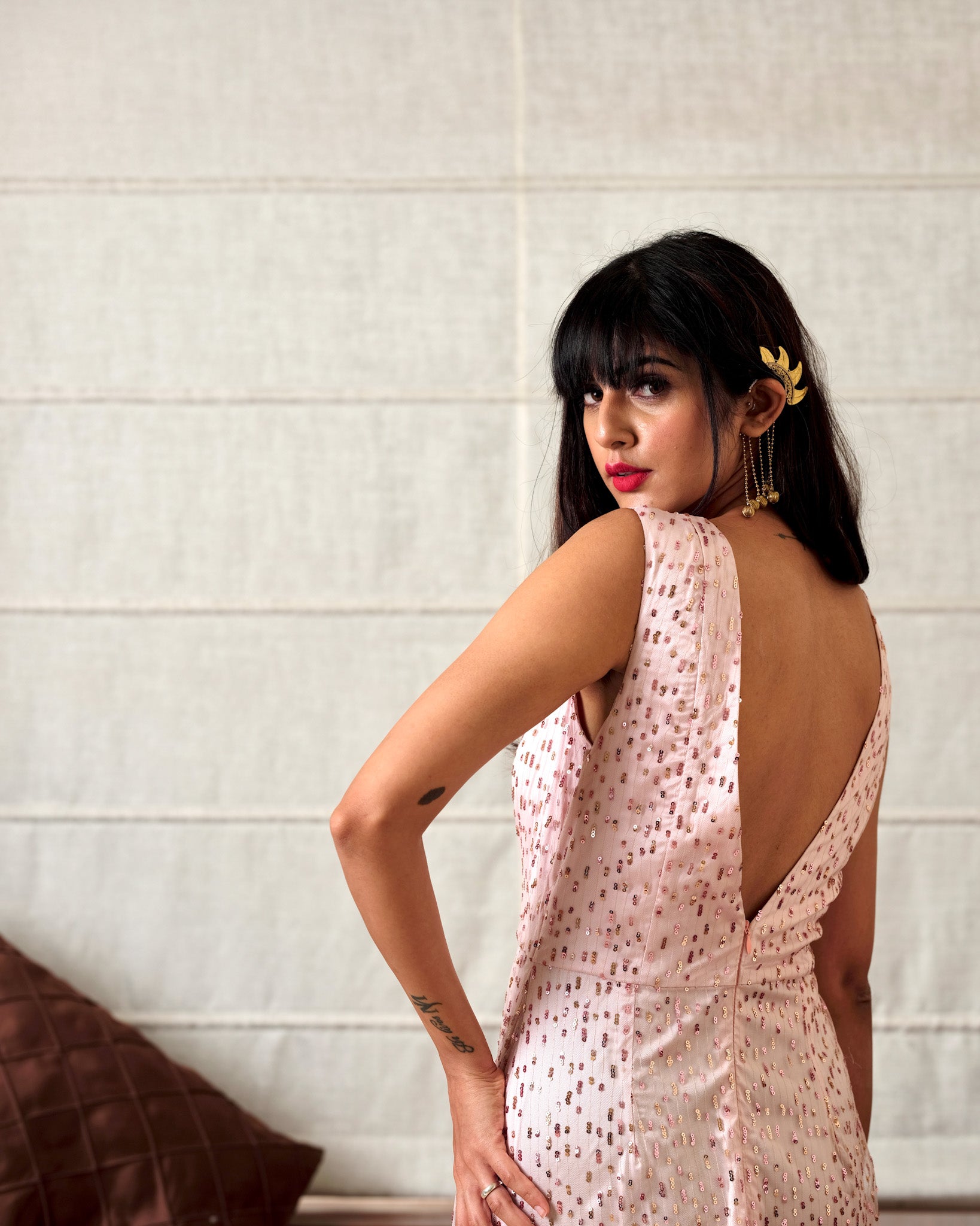 Woman wearing a light pink dress with a backless design, standing against a neutral wall.