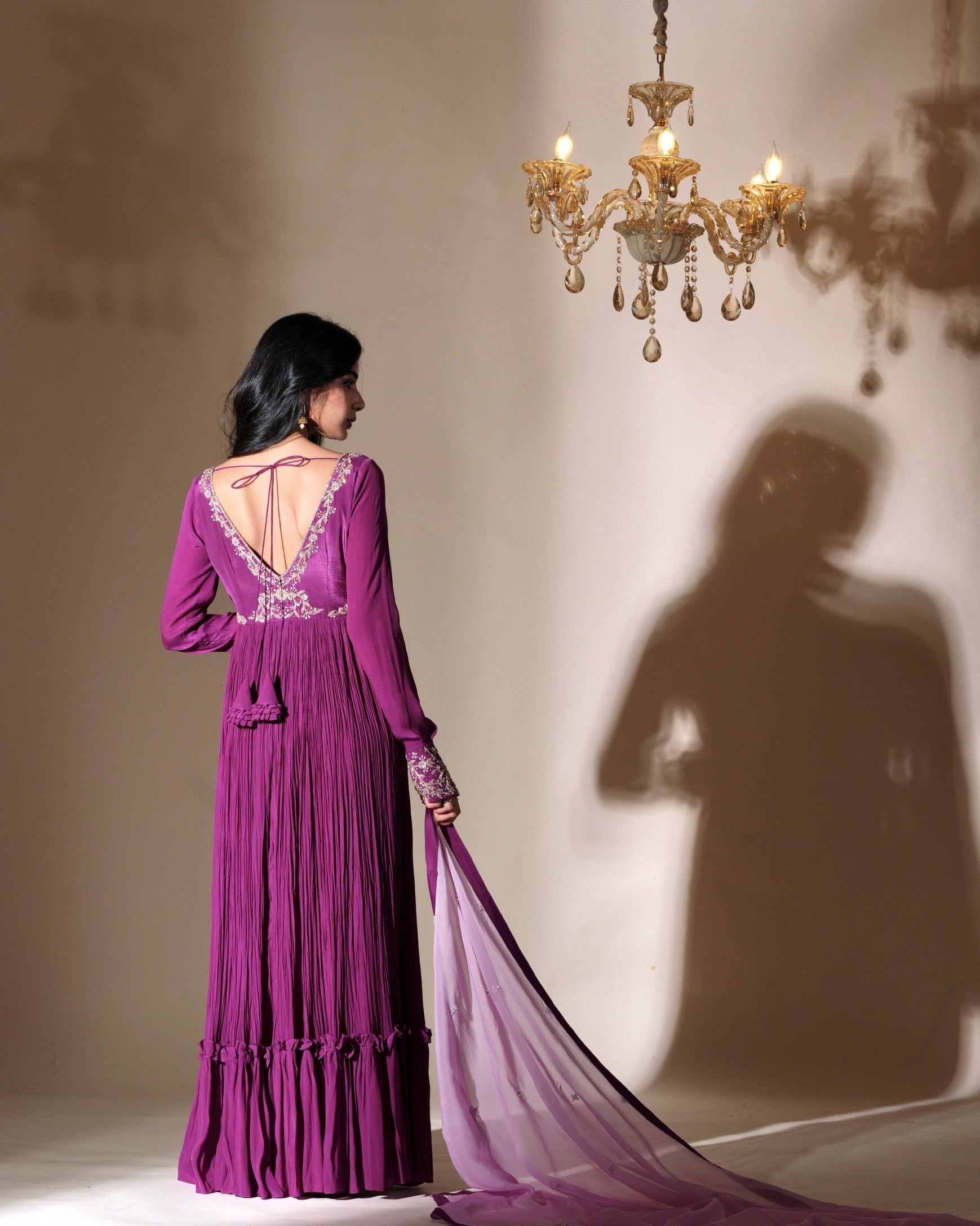 Woman in a purple evening gown with a chandelier casting a shadow on the wall.